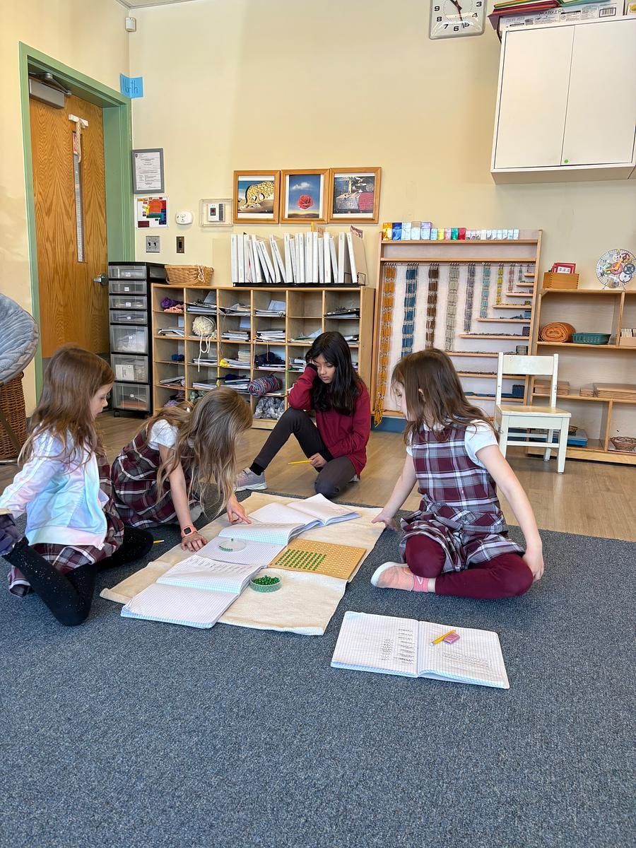 Four children and a teacher examining materials on a rug in a classroom.