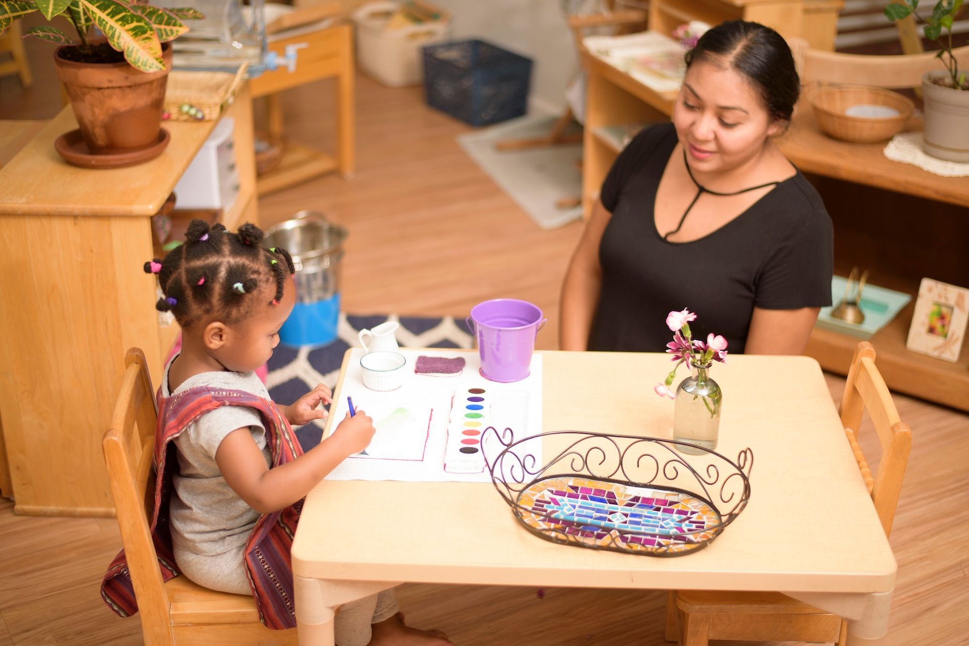Child and woman seated at a small table, crafting with colorful supplies in a cozy room