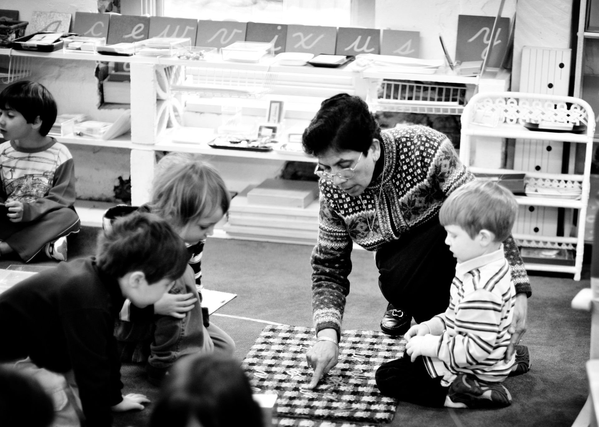 A Montessori teacher engaging with a group of children on the floor, using a mat for a lesson in a warm and inviting classroom.