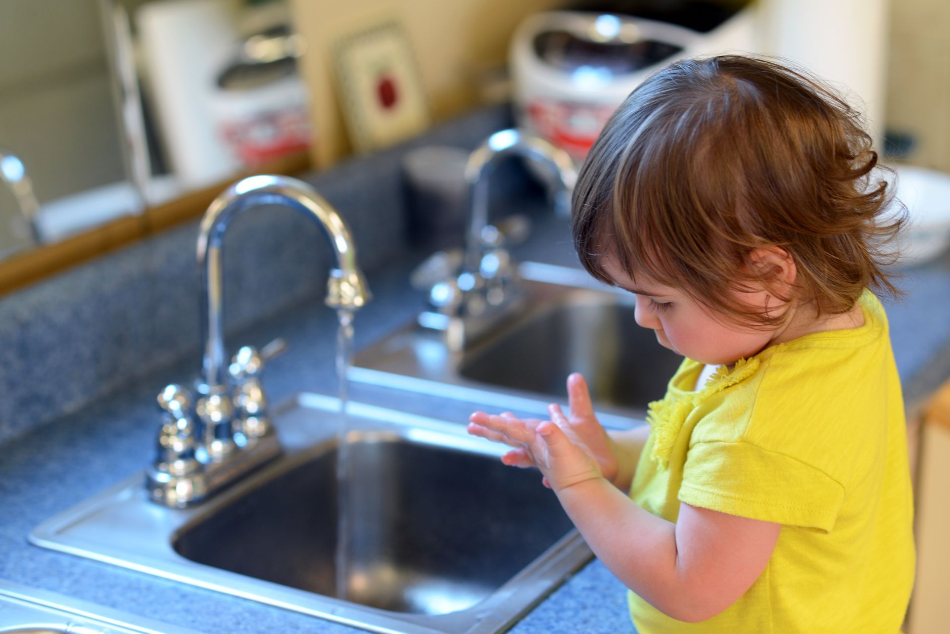 A young child in a Montessori classroom washing hands at a sink, practicing practical life skills.