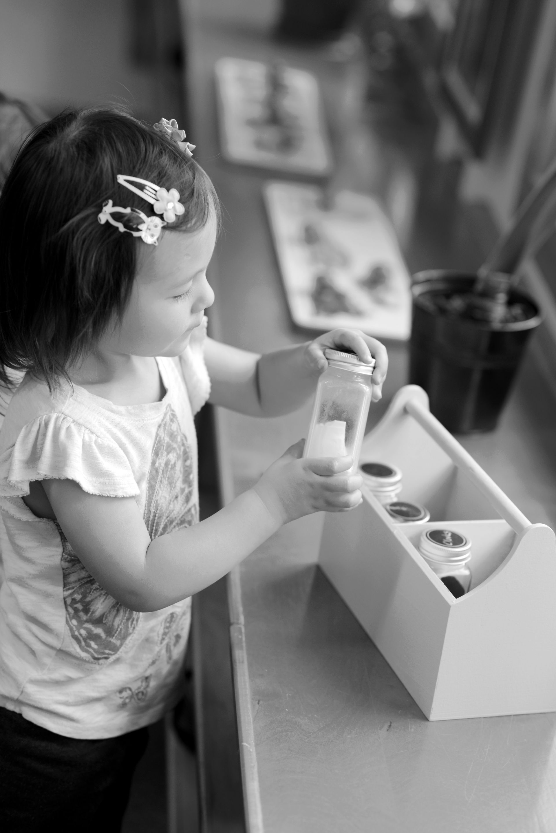 A young girl in a Montessori classroom carefully examining a small jar from a set of sensory materials.