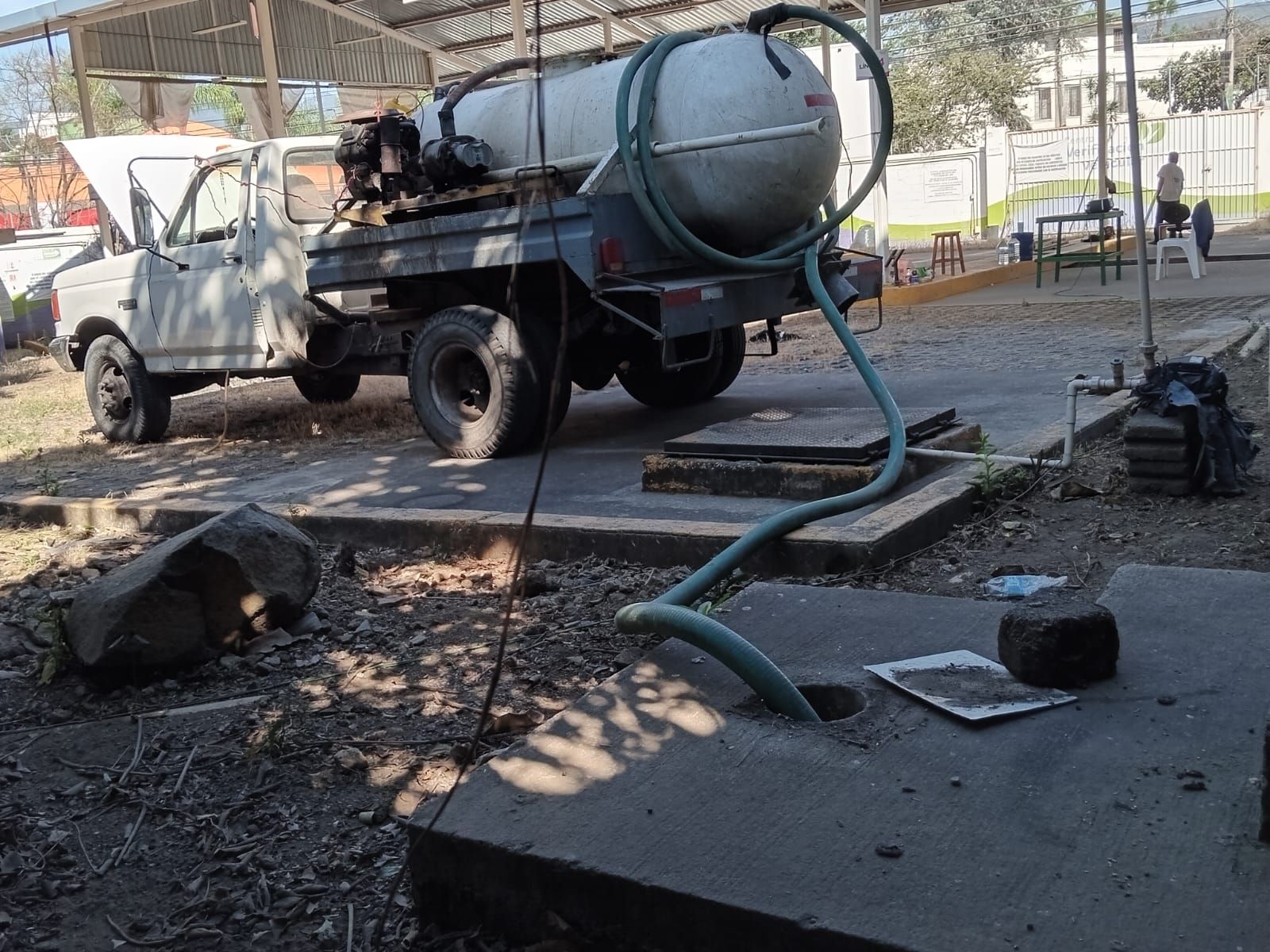 Un camión con cisterna y manguera conectado a una fosa séptica de hormigón. Escenario al aire libre.