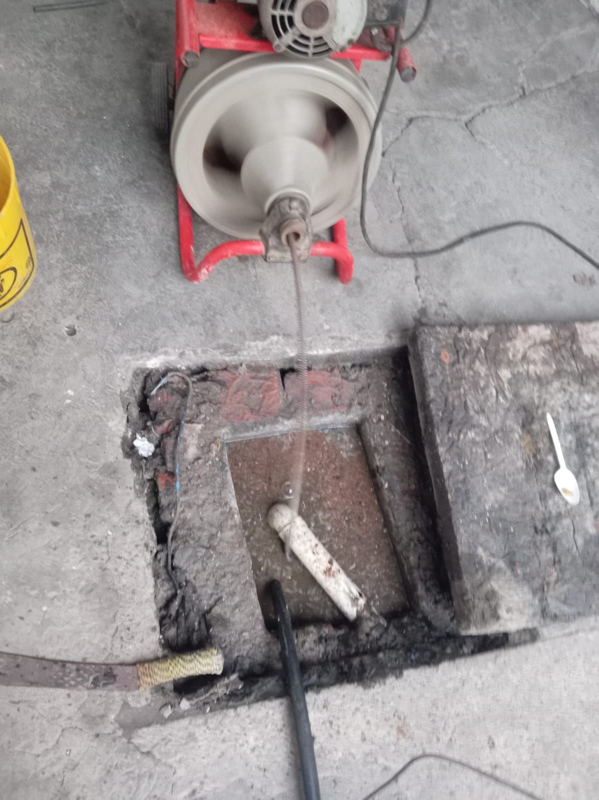 Máquina desatascadora de plomería en uso cerca de un punto de acceso a alcantarillado abierto.