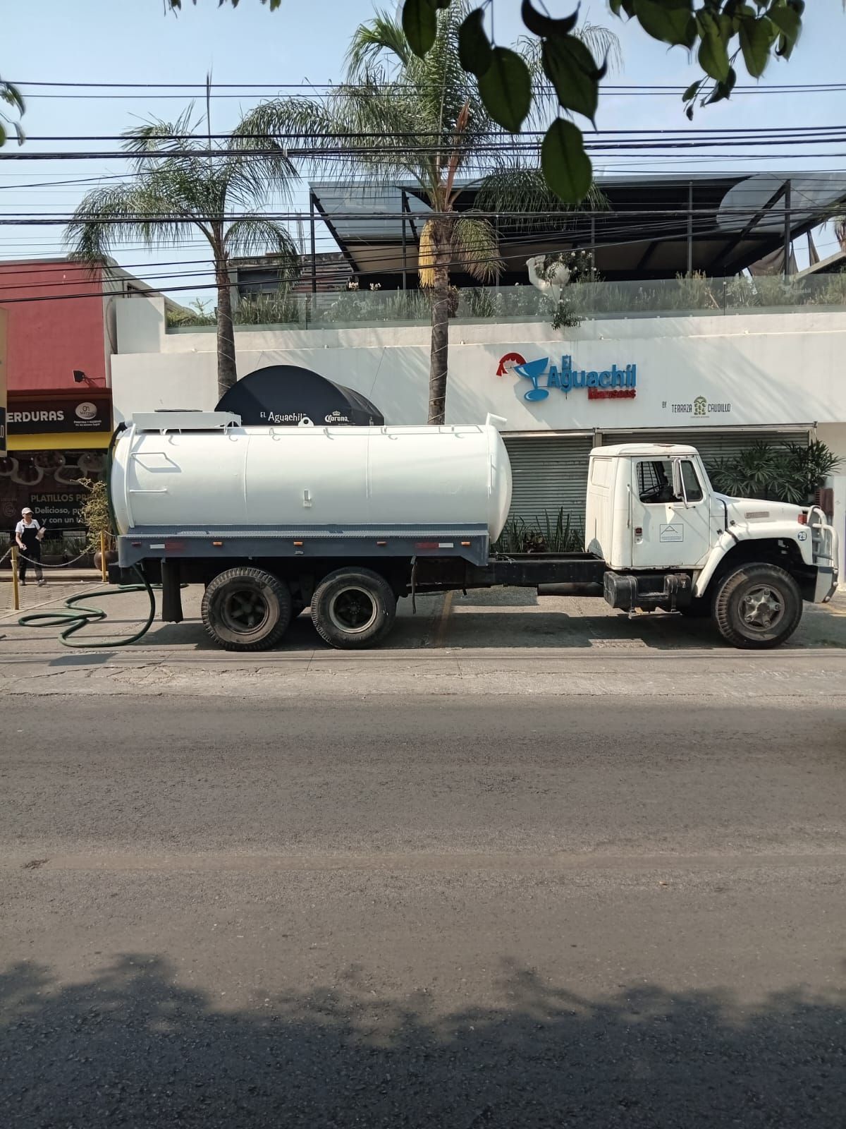Camión cisterna de agua blanca estacionado en una calle cerca de un edificio con la palabra