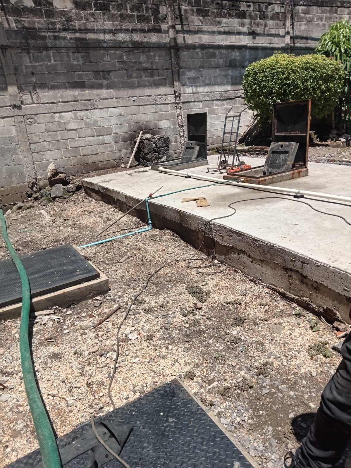 Plataforma de hormigón en una obra en construcción con herramientas, tuberías y un fondo de pared de ladrillo.