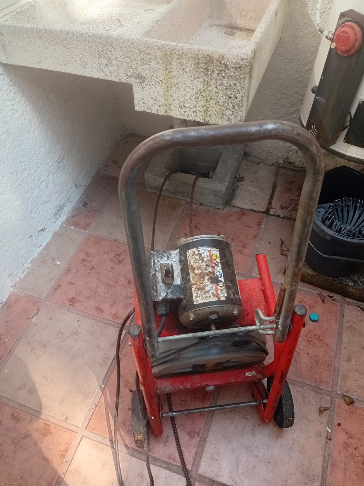Hidrolavadora roja y negra sobre un patio embaldosado cerca de un fregadero de hormigón.