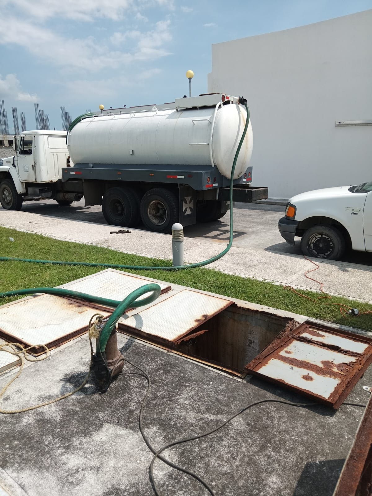 Camión con manguera cisterna conectada a un punto de acceso subterráneo abierto.