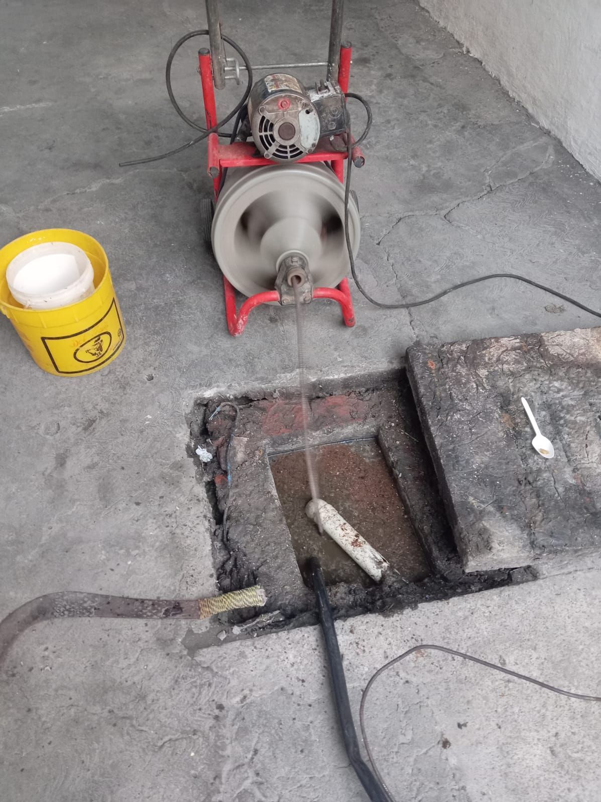 Máquina de limpieza de alcantarillado en uso, con un cable giratorio insertado en un punto de acceso abierto sobre hormigón.