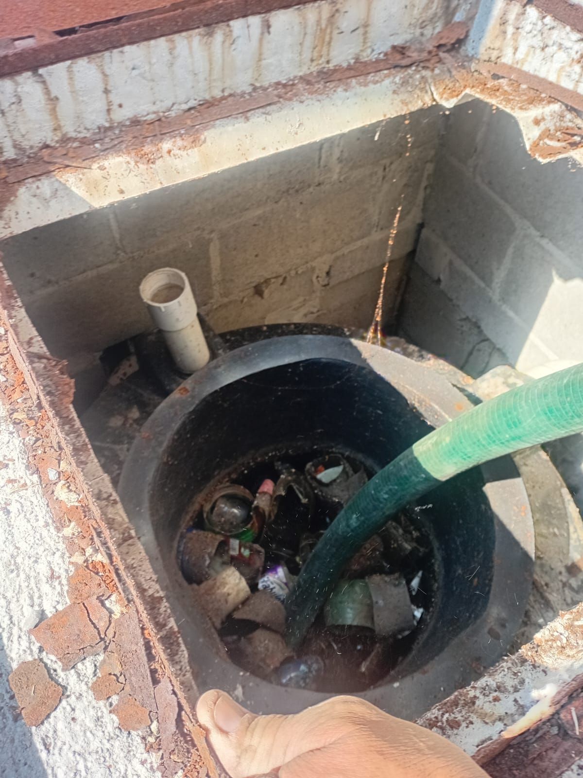 Una manguera llena un tanque lleno de basura dentro de una abertura revestida de ladrillos en un tejado.