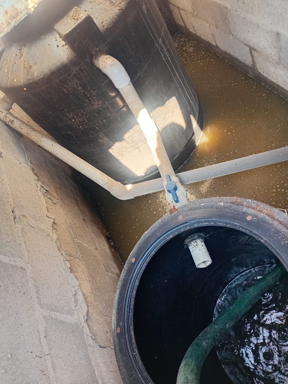Interior de tanque séptico abierto con tuberías y neumático en agua turbia.