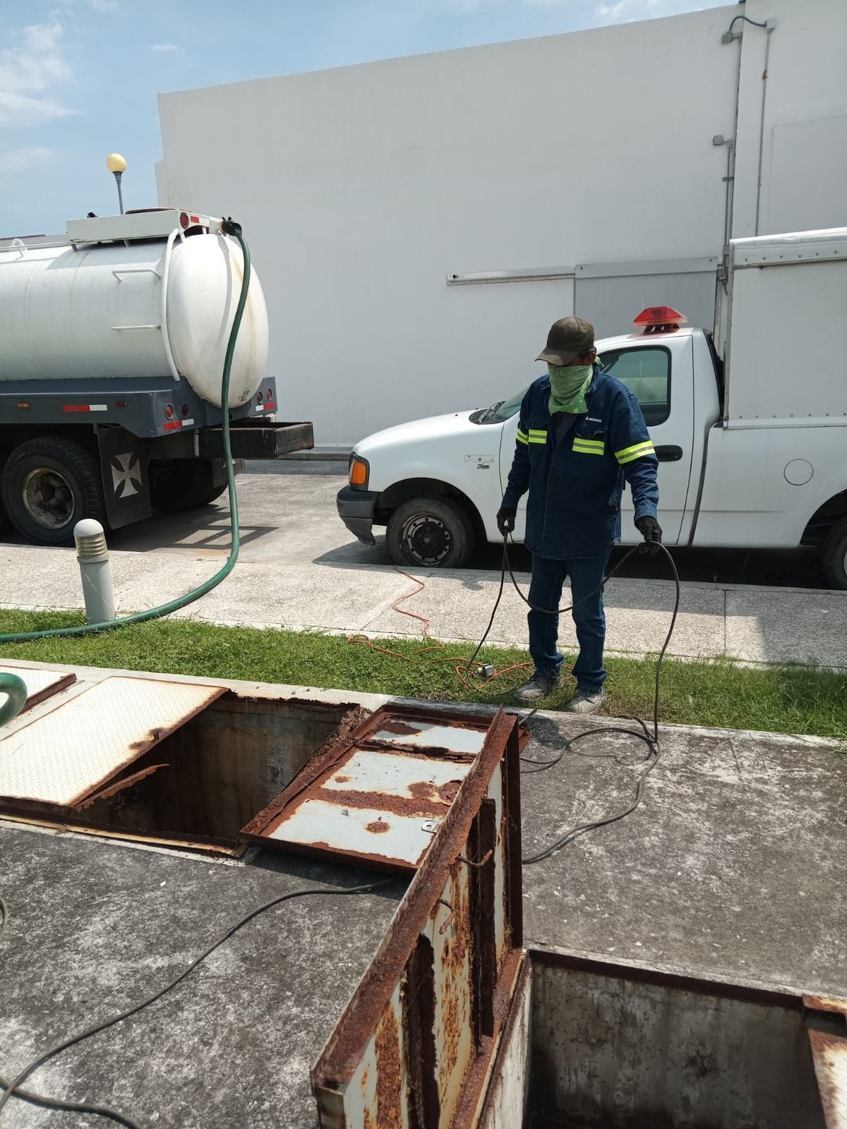 Hombre uniformado cerca de un tanque abierto; camión blanco y camión cisterna visibles; entorno industrial.