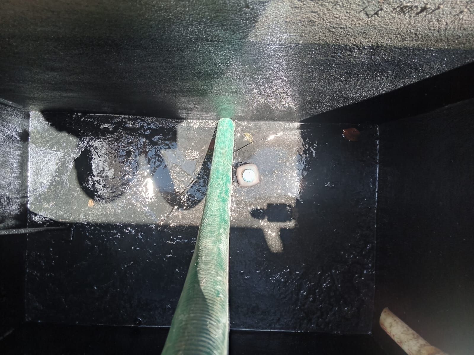 Dentro de un tanque oscuro y recién pintado, una manguera verde rocía agua.
