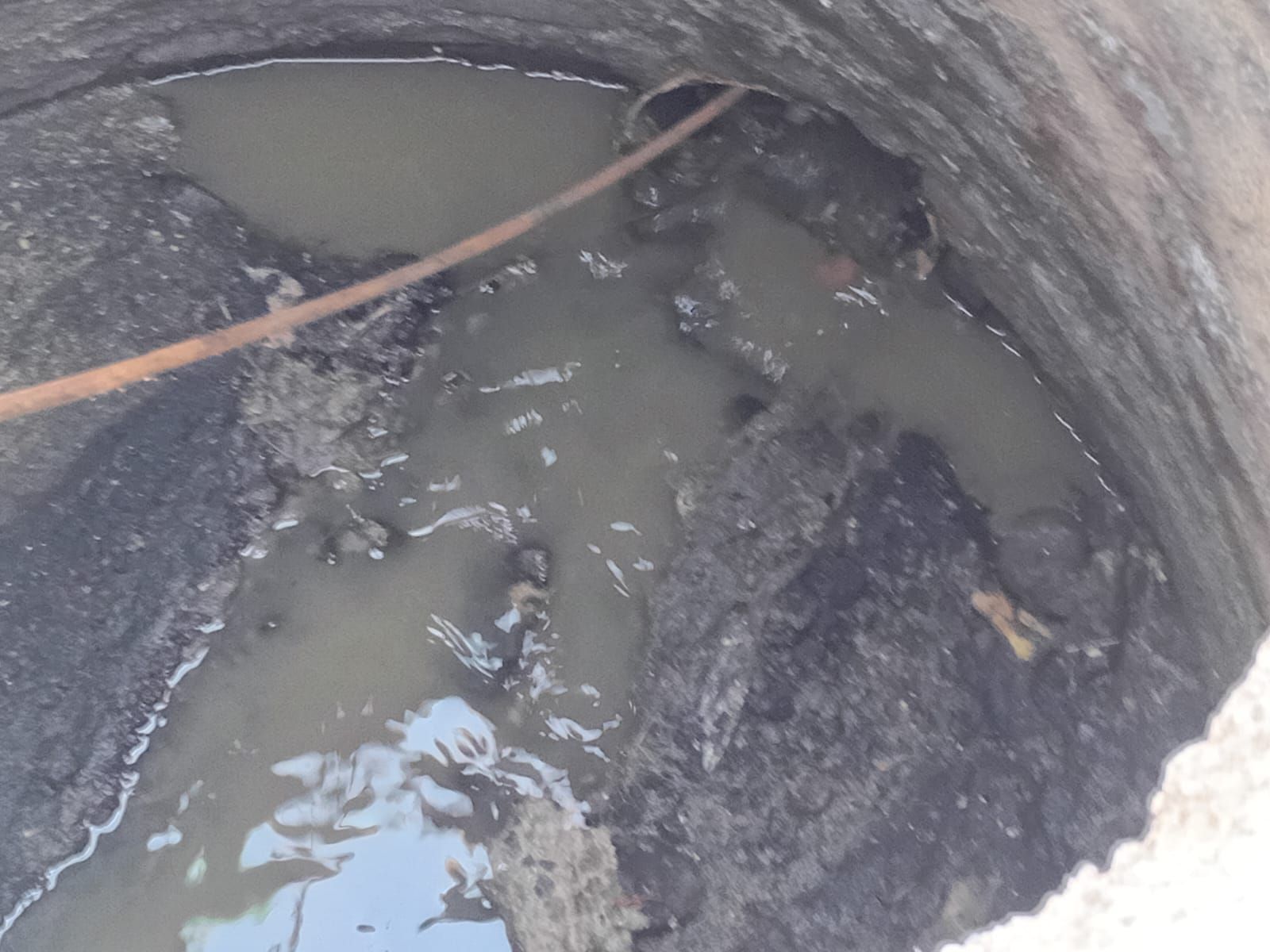 Mirando hacia abajo a un pozo sucio y lleno de agua con una tubería oxidada y escombros.