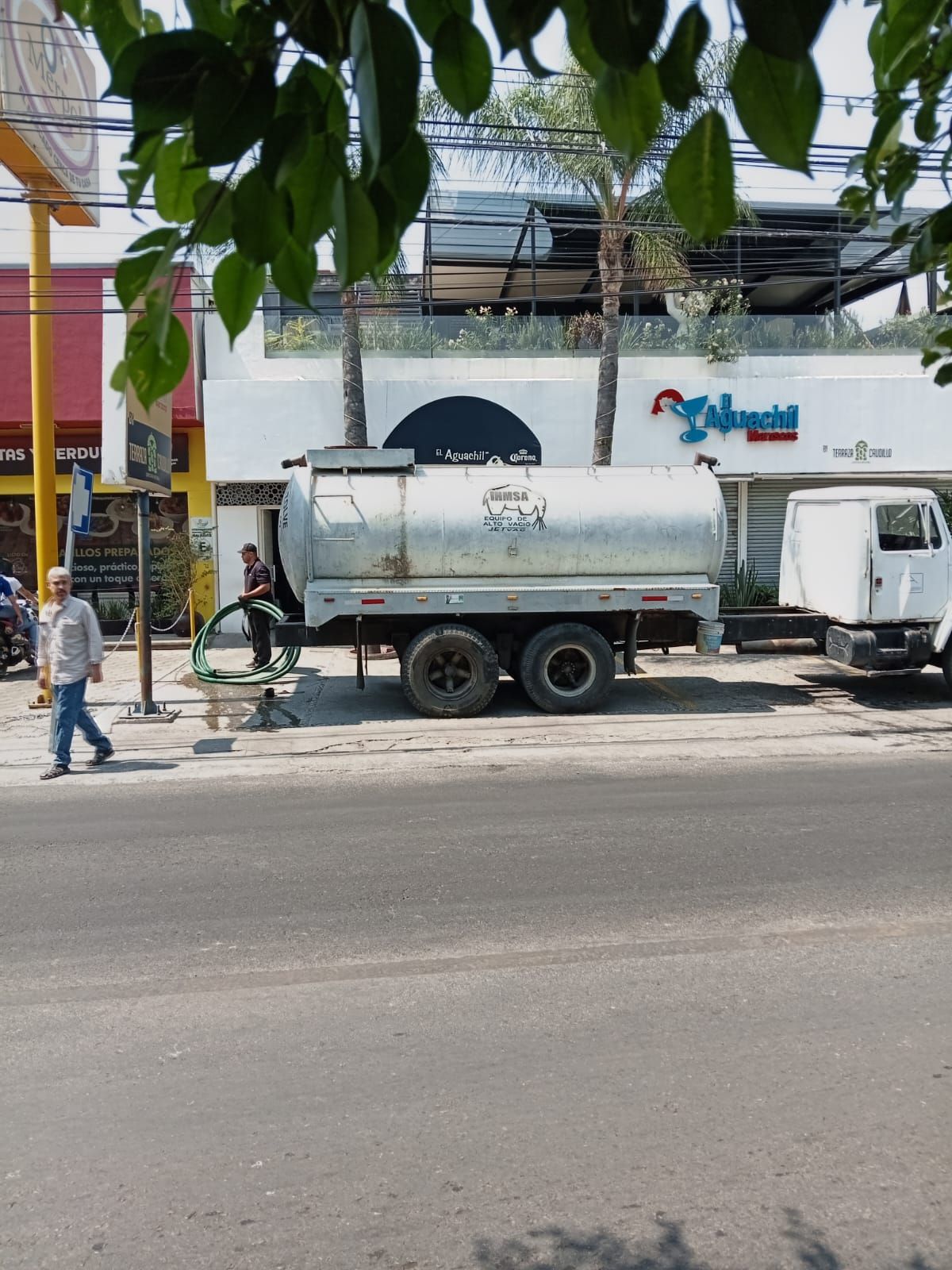 Camión cisterna estacionado cerca de un edificio. Una persona conecta una manguera. Calle enfrente.