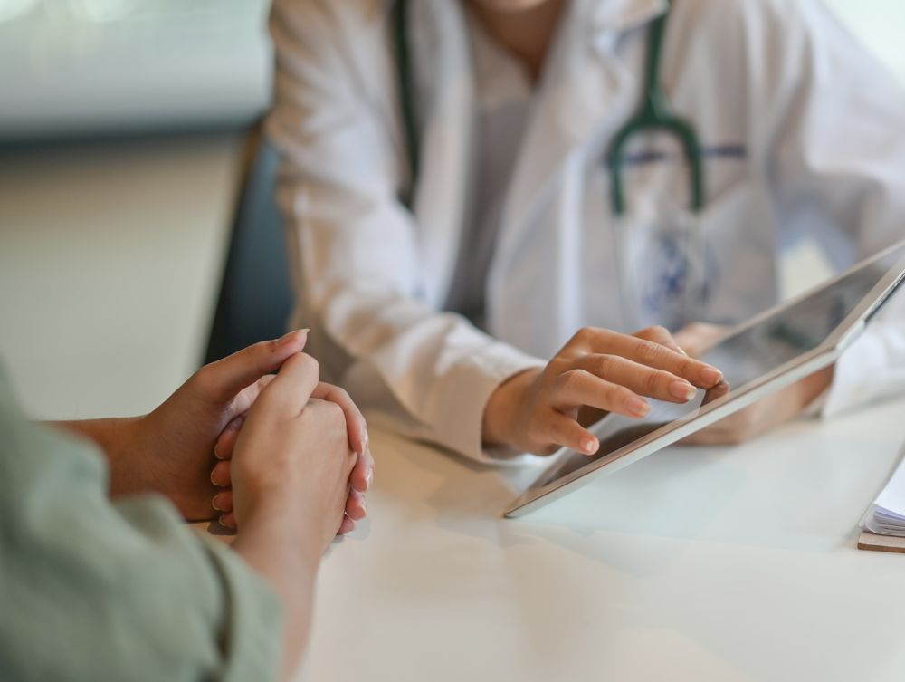 A doctor is talking to a patient while using a tablet computer.