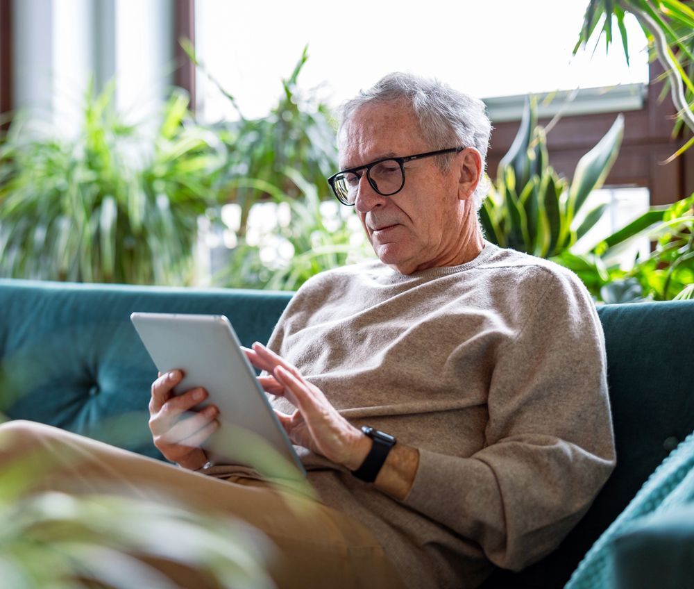 An older man is sitting on a couch using a tablet computer.