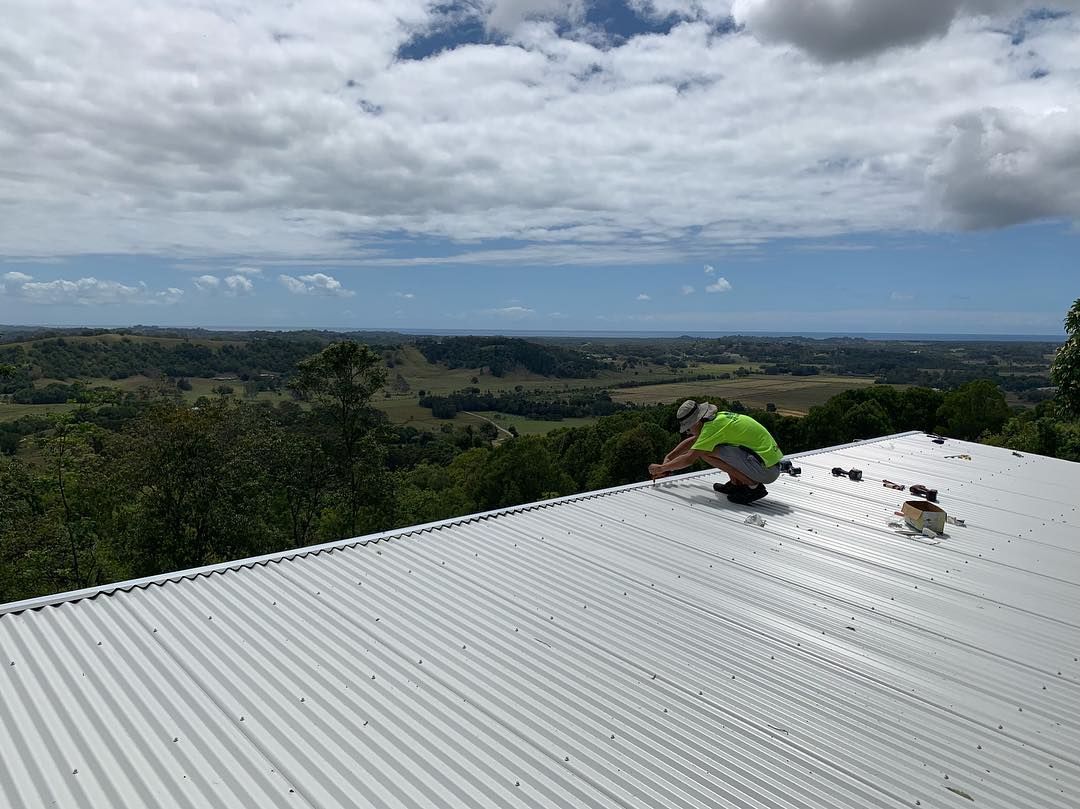 A Man is Working on the Roof of a Building — Northern Rivers Metal Roofing PTY LTD In Ewingsdale, NSW
