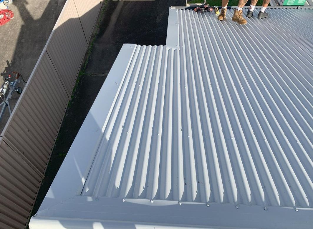 A Person is Standing on the Roof of a Building — Northern Rivers Metal Roofing PTY LTD In Byron Bay , NSW