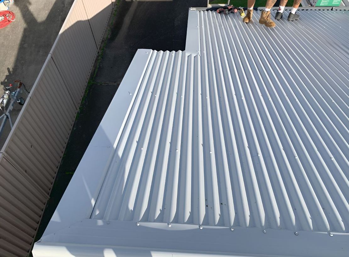 A Person is Standing on the Roof of a Building — Northern Rivers Metal Roofing PTY LTD In Pottsville, NSW