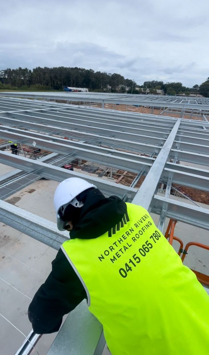 A Man in a Yellow Vest is Working on a Metal Structure — Northern Rivers Metal Roofing PTY LTD In Alstonville, NSW