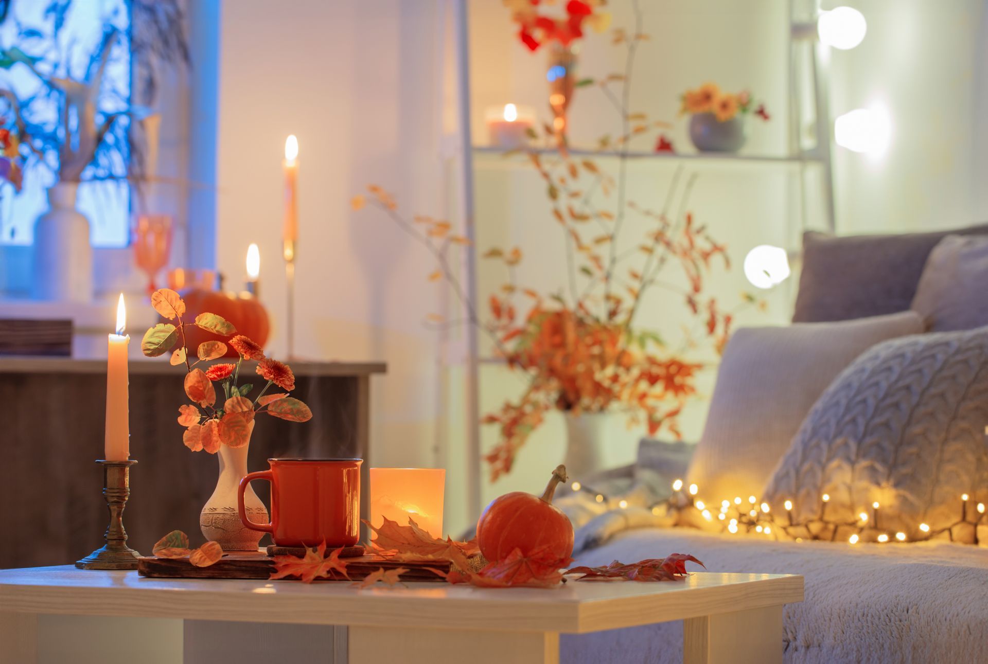 A living room decorated for autumn with candles , pumpkins , leaves and a couch.