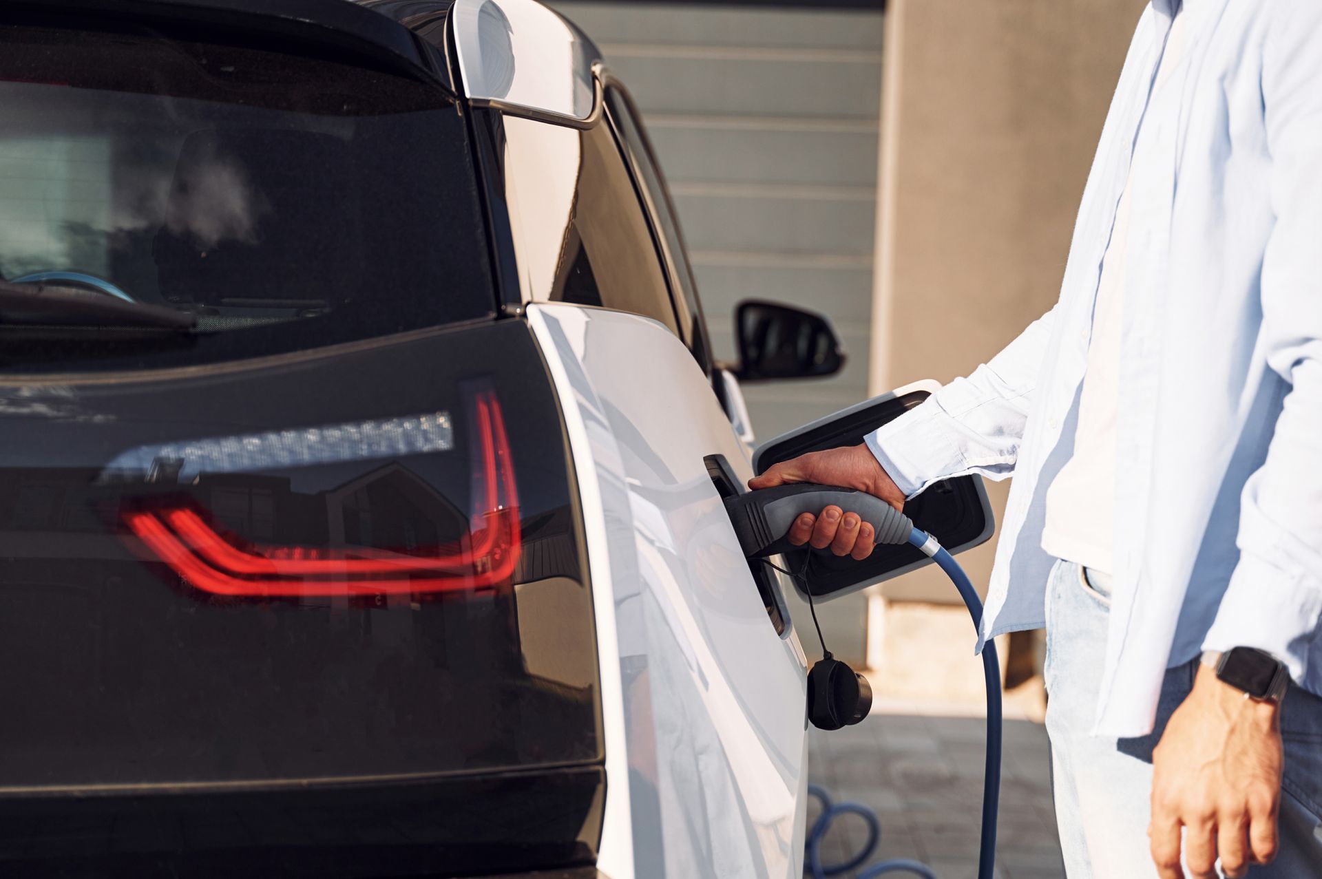 Person plugging an electric car into a charger. Car is black and white, outdoors.