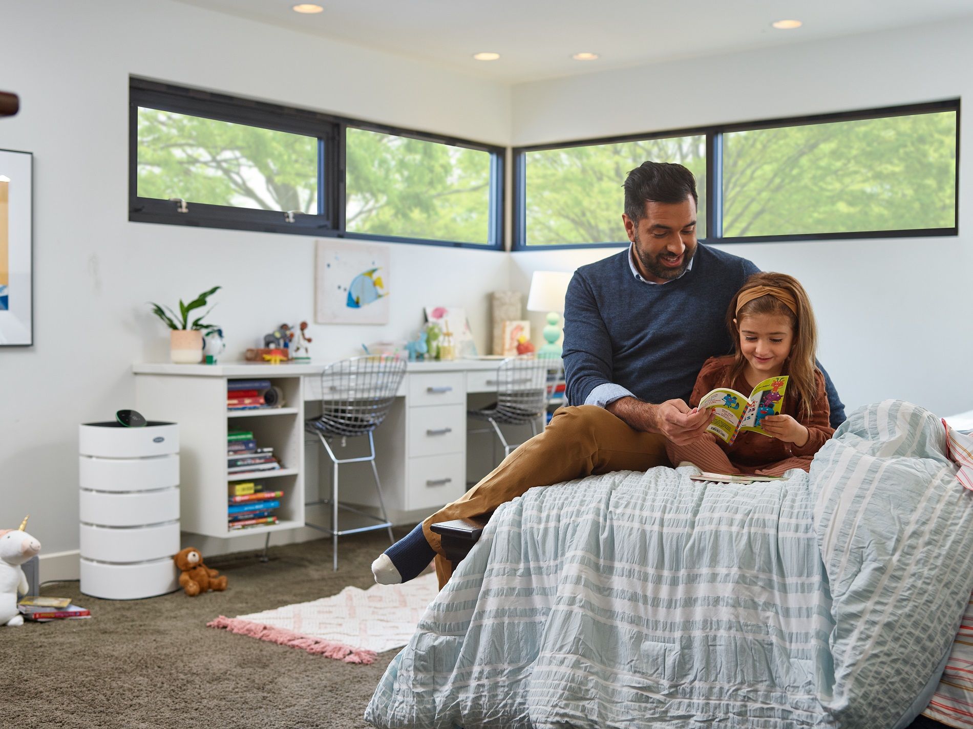 Father and child reading a book together in a bedroom with a desk and air purifier.
