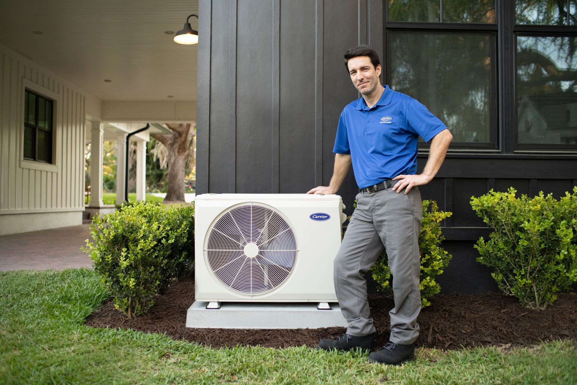 A man is standing next to a large air conditioner outside of a house.