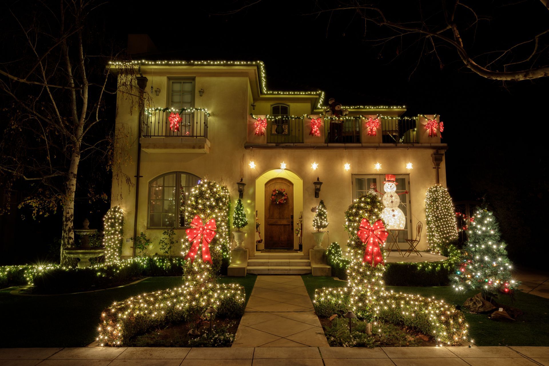 House decorated with Christmas lights, featuring garland and large light displays, at night.