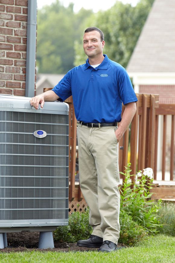 Man in blue polo stands by an air conditioning unit outside a brick building.