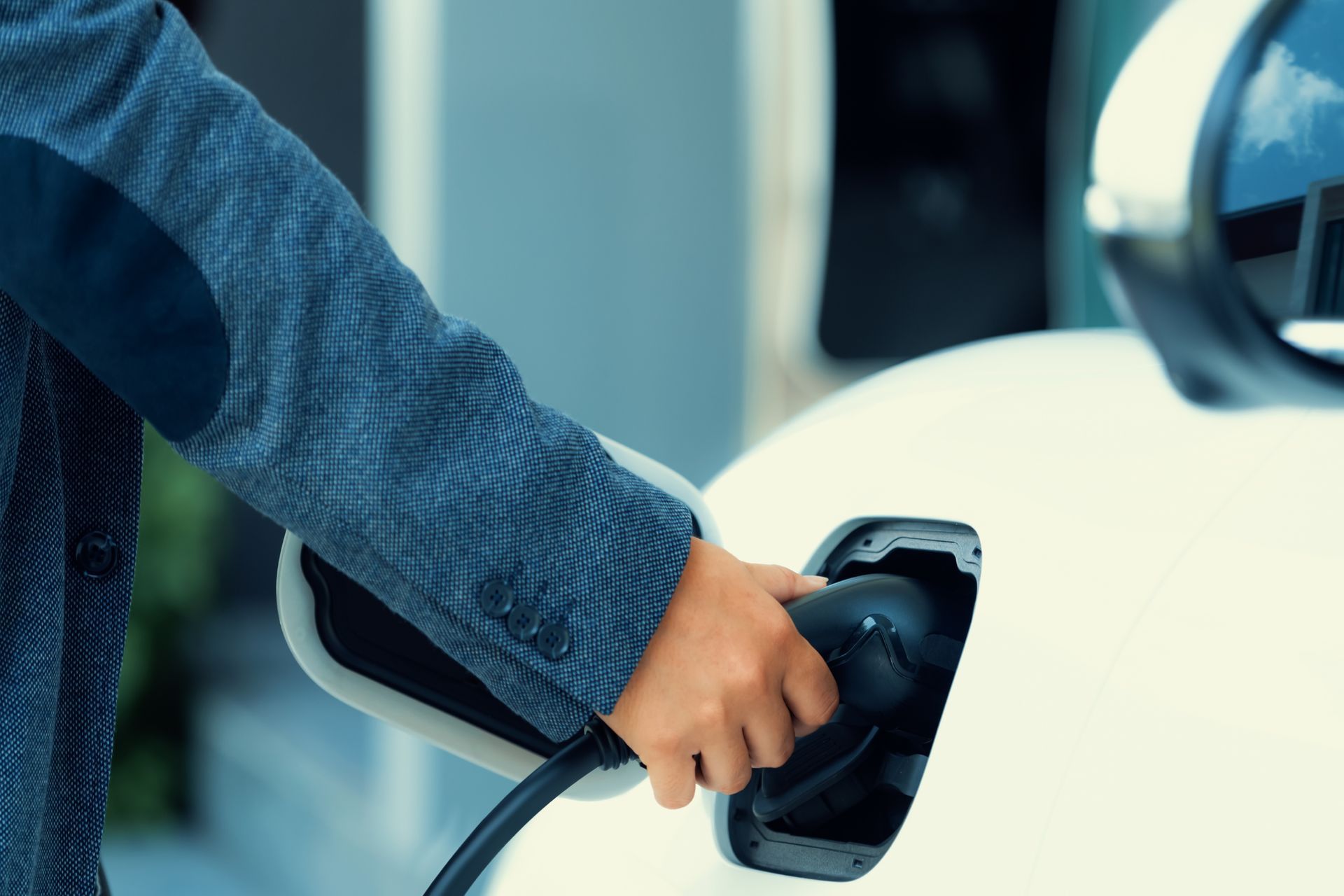 Person plugging an electric vehicle charging cable into a white car.