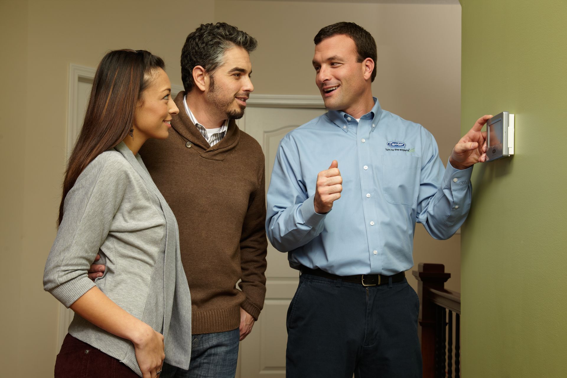 Man in uniform shows thermostat to a couple indoors.