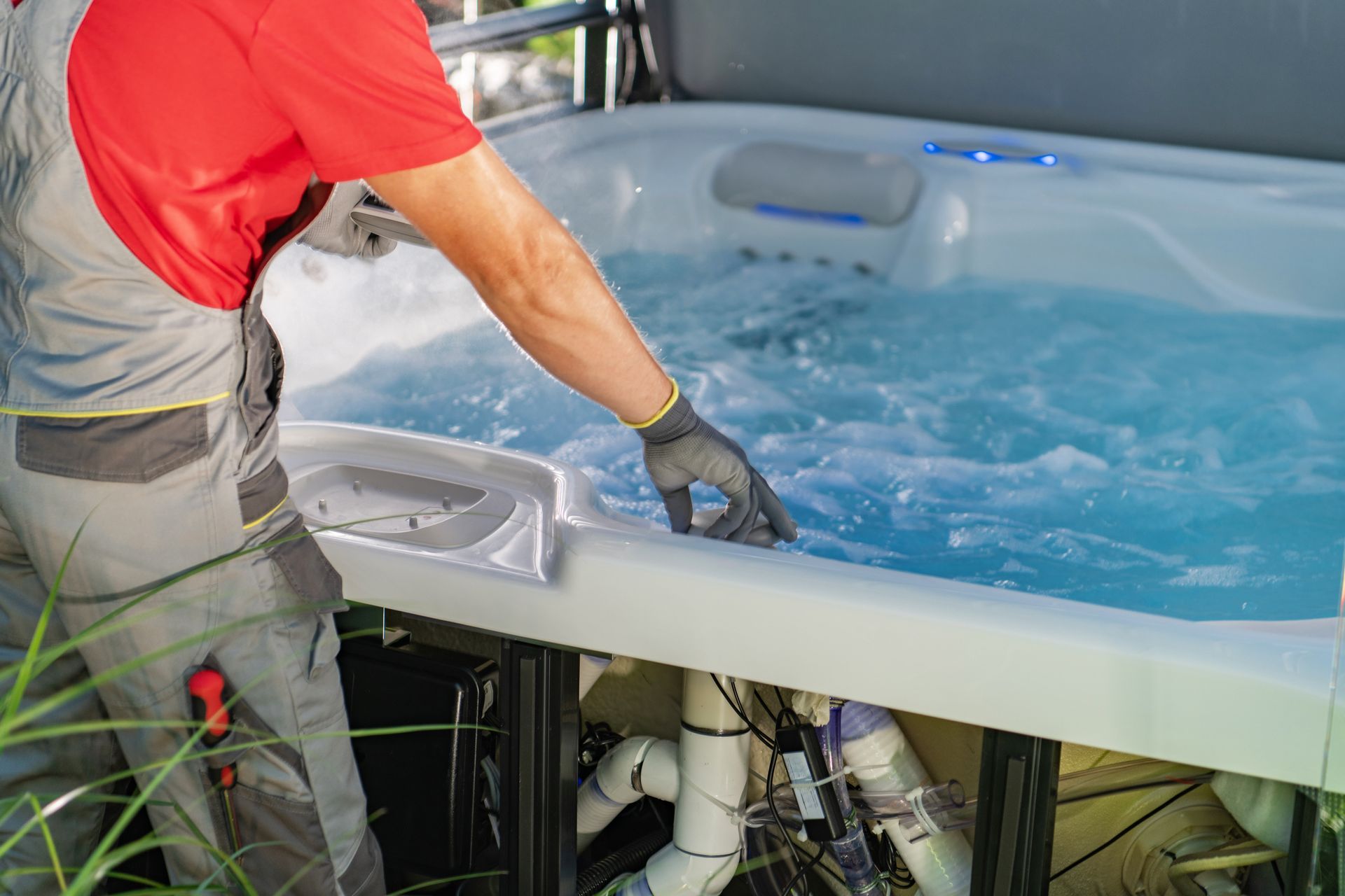 A person in work uniform inspects the water and exposed piping of a bubbling hot tub.