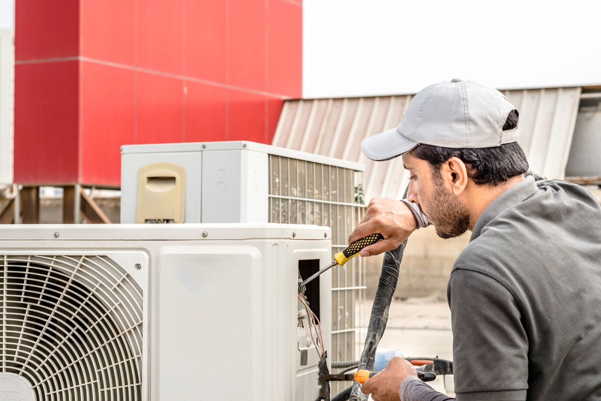 A man is fixing an air conditioner with a screwdriver.