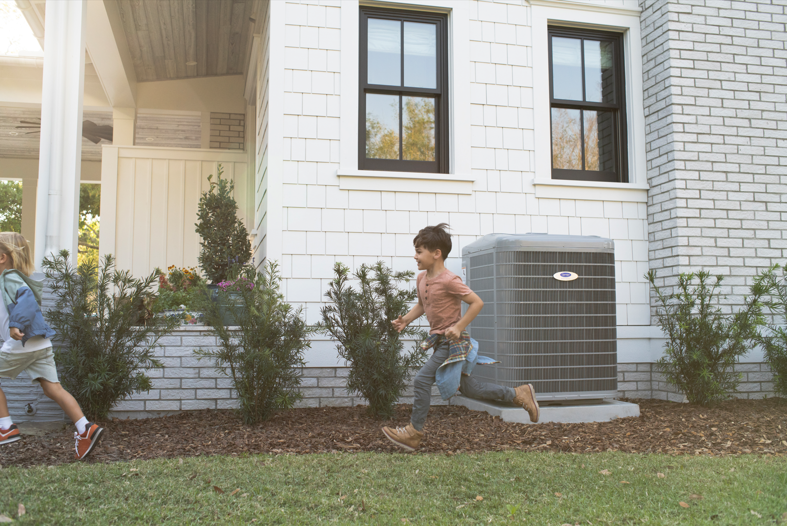 A boy and a girl are running in front of a white brick house.