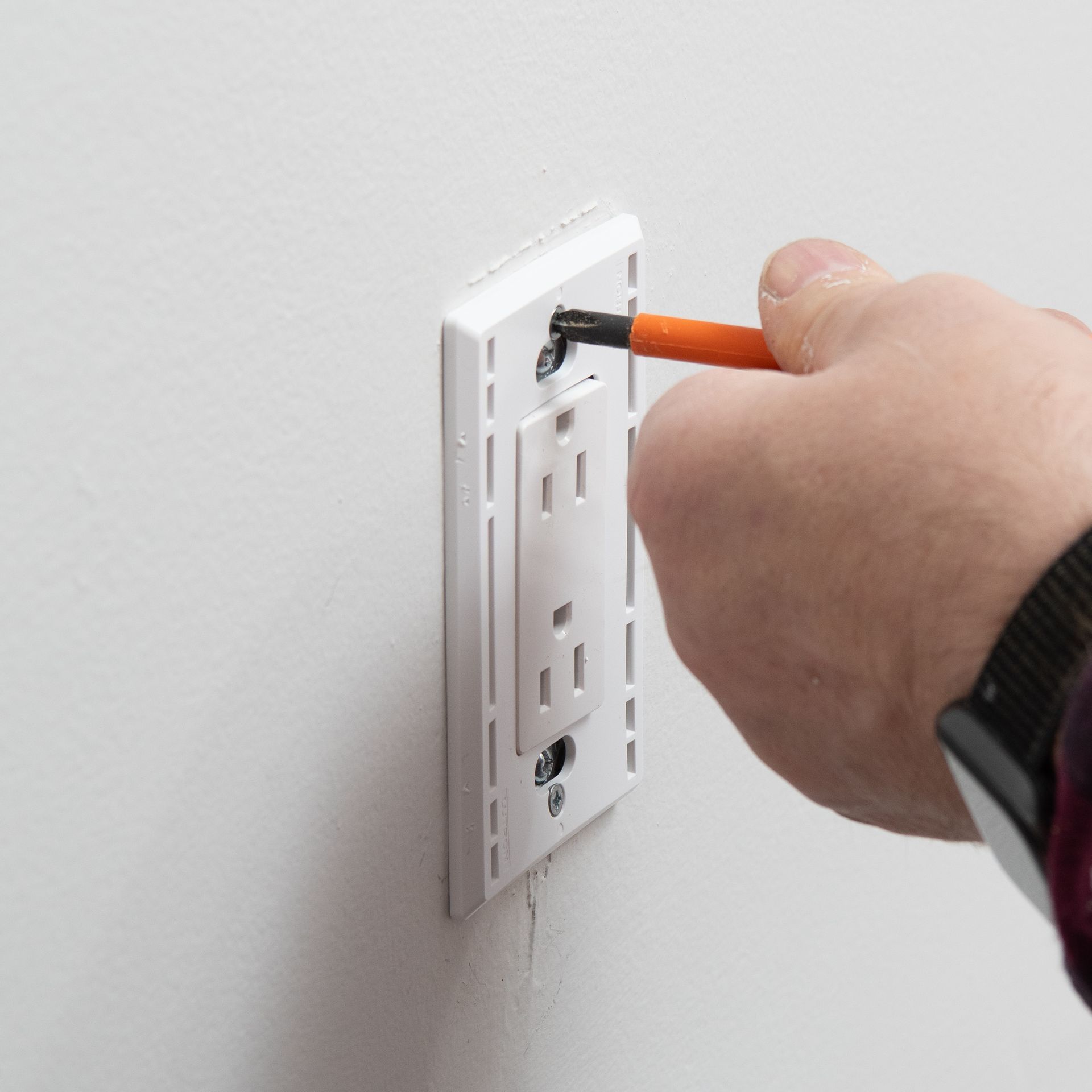 a person is installing an electrical outlet on a wall with a screwdriver .