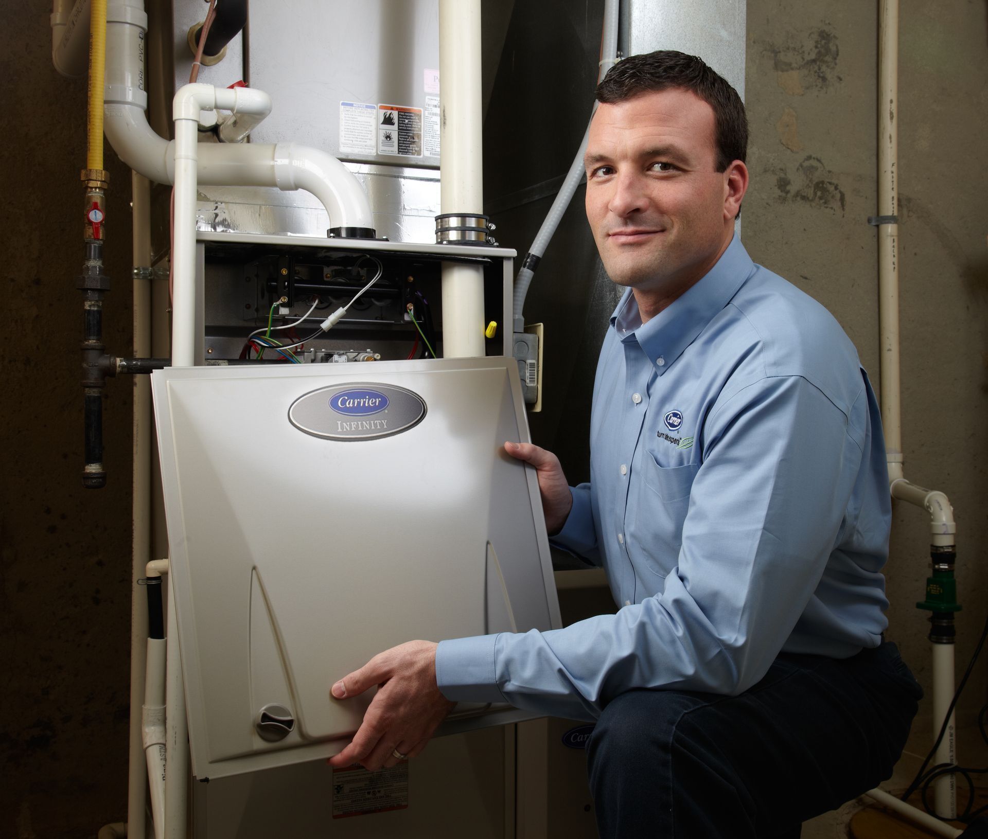 A man in a blue shirt is kneeling in front of an air conditioner