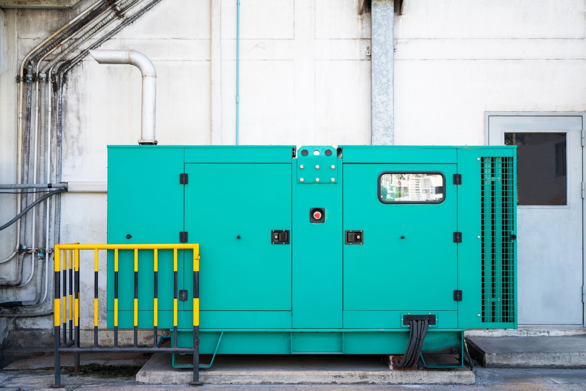 A large green generator is parked in front of a building.