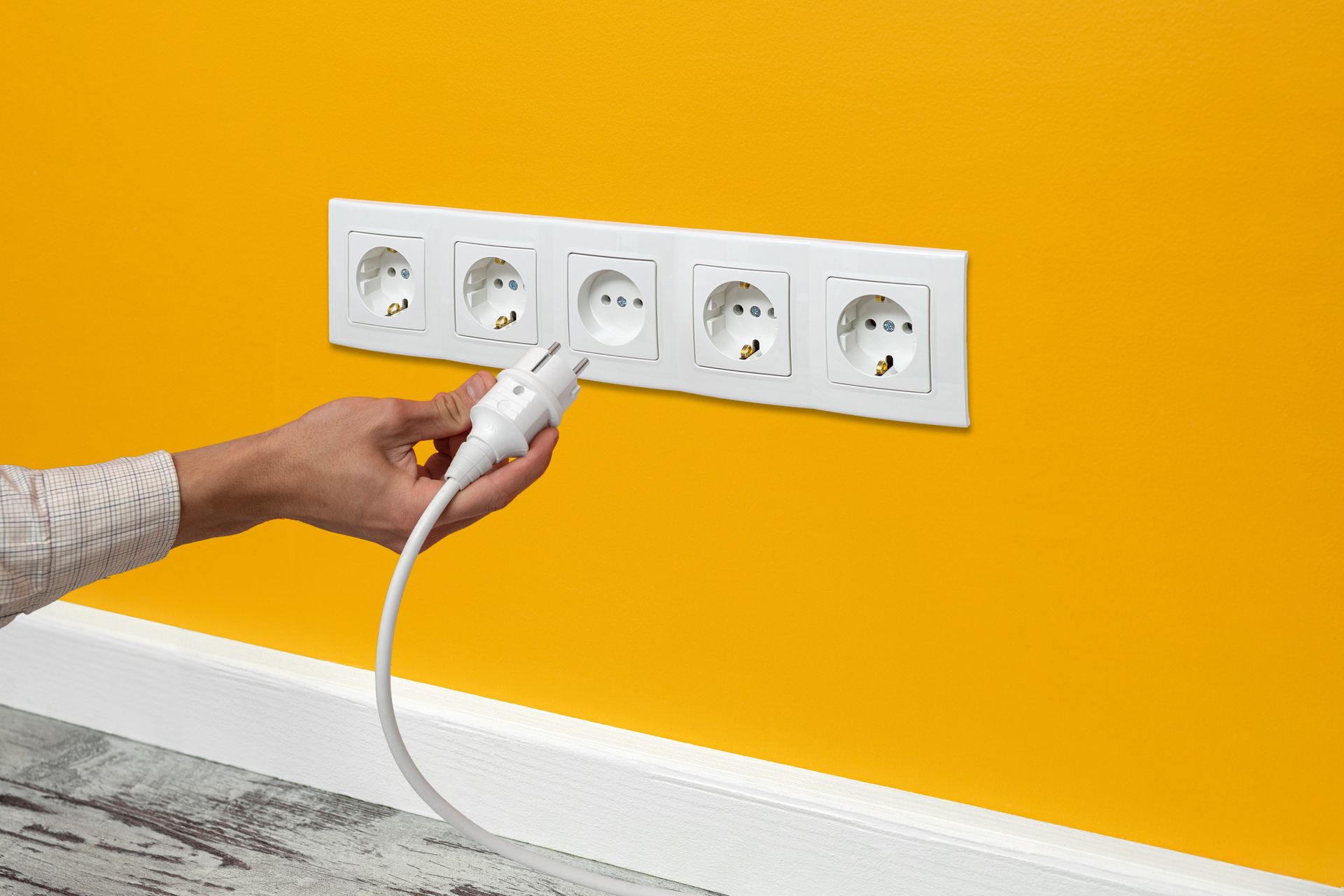 a person is plugging a cord into an electrical outlet on a yellow wall .