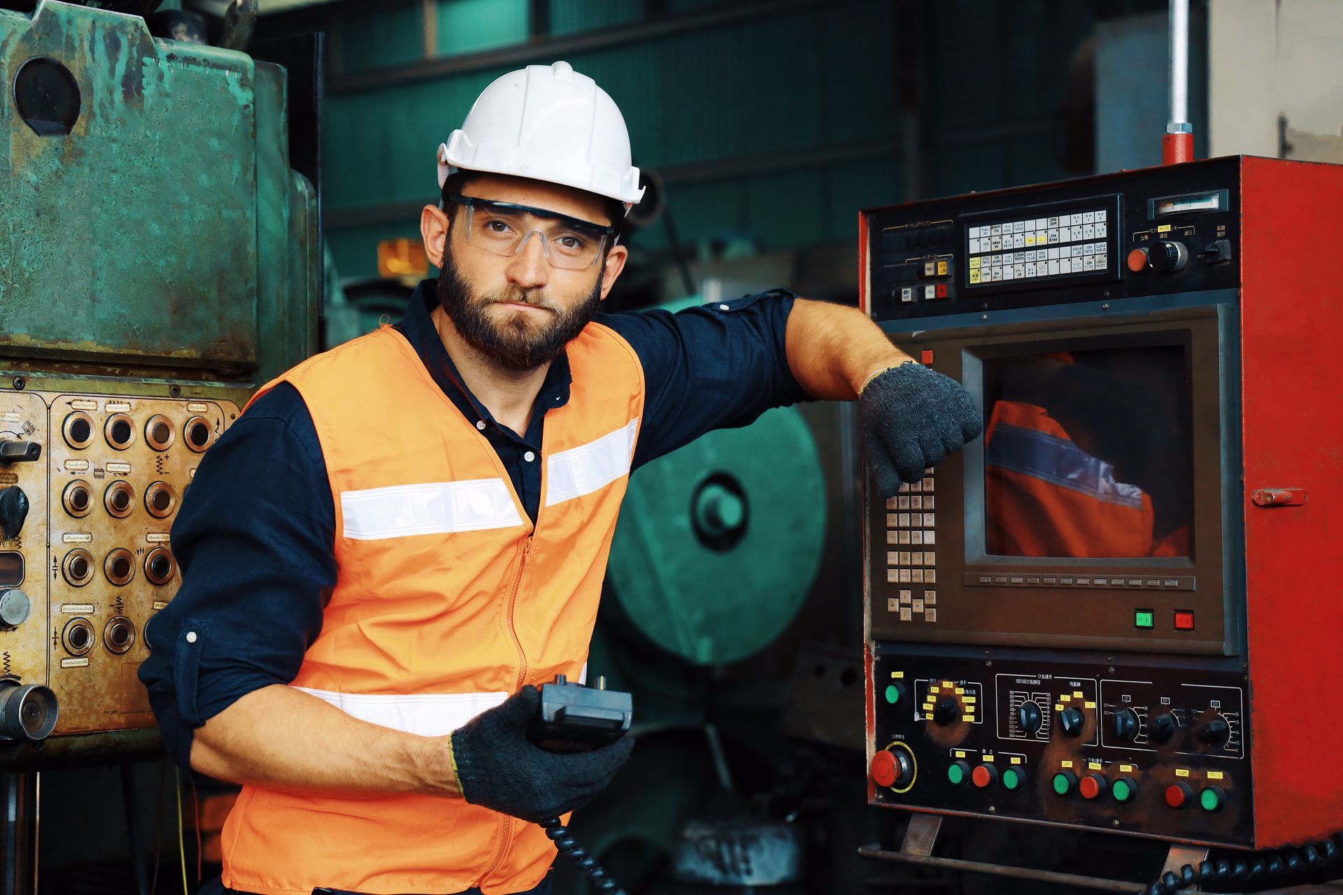 a man wearing a hard hat and safety glasses is standing in front of a machine in a factory .