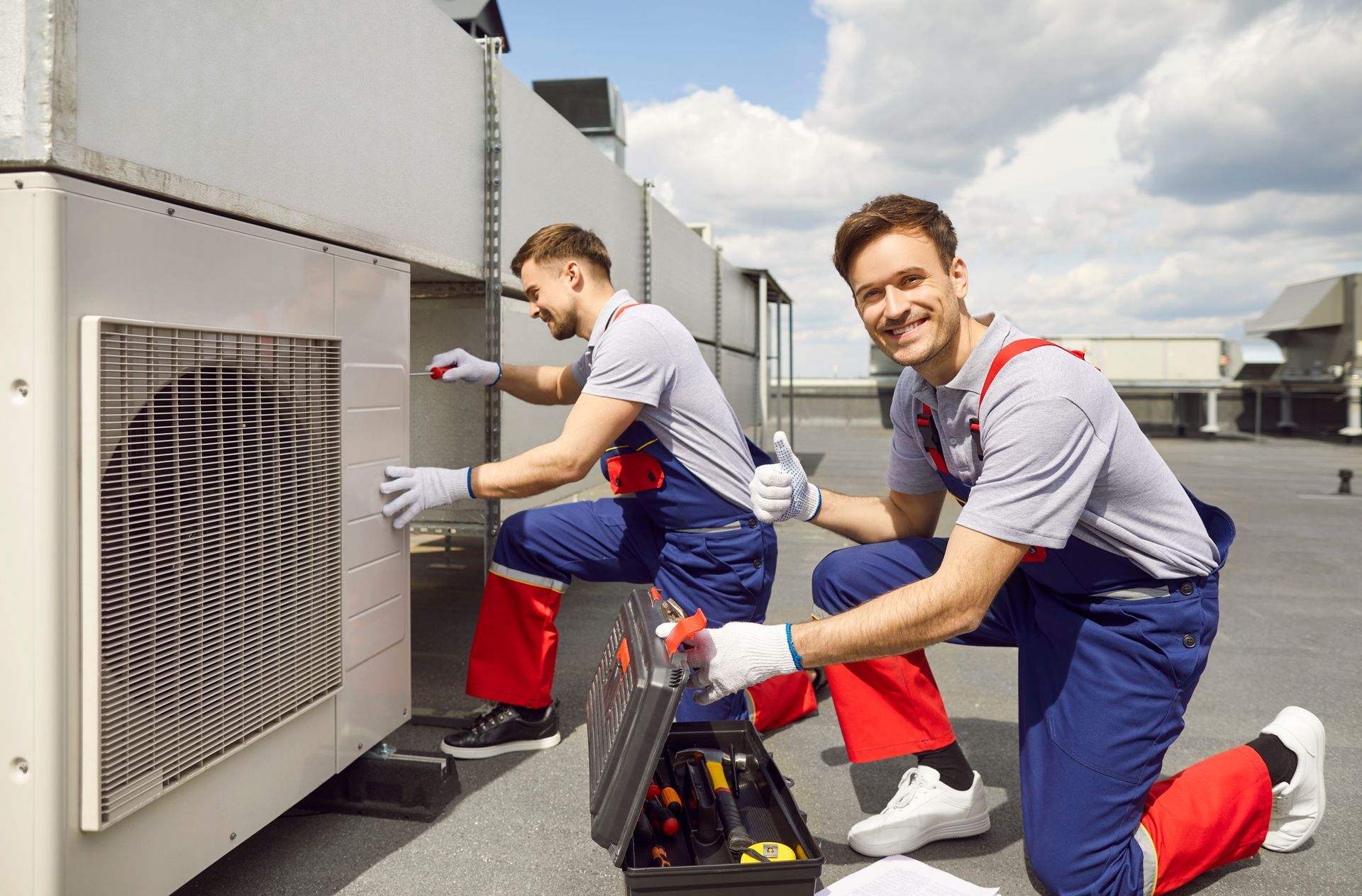 Two men are working on an air conditioner on the roof of a building.