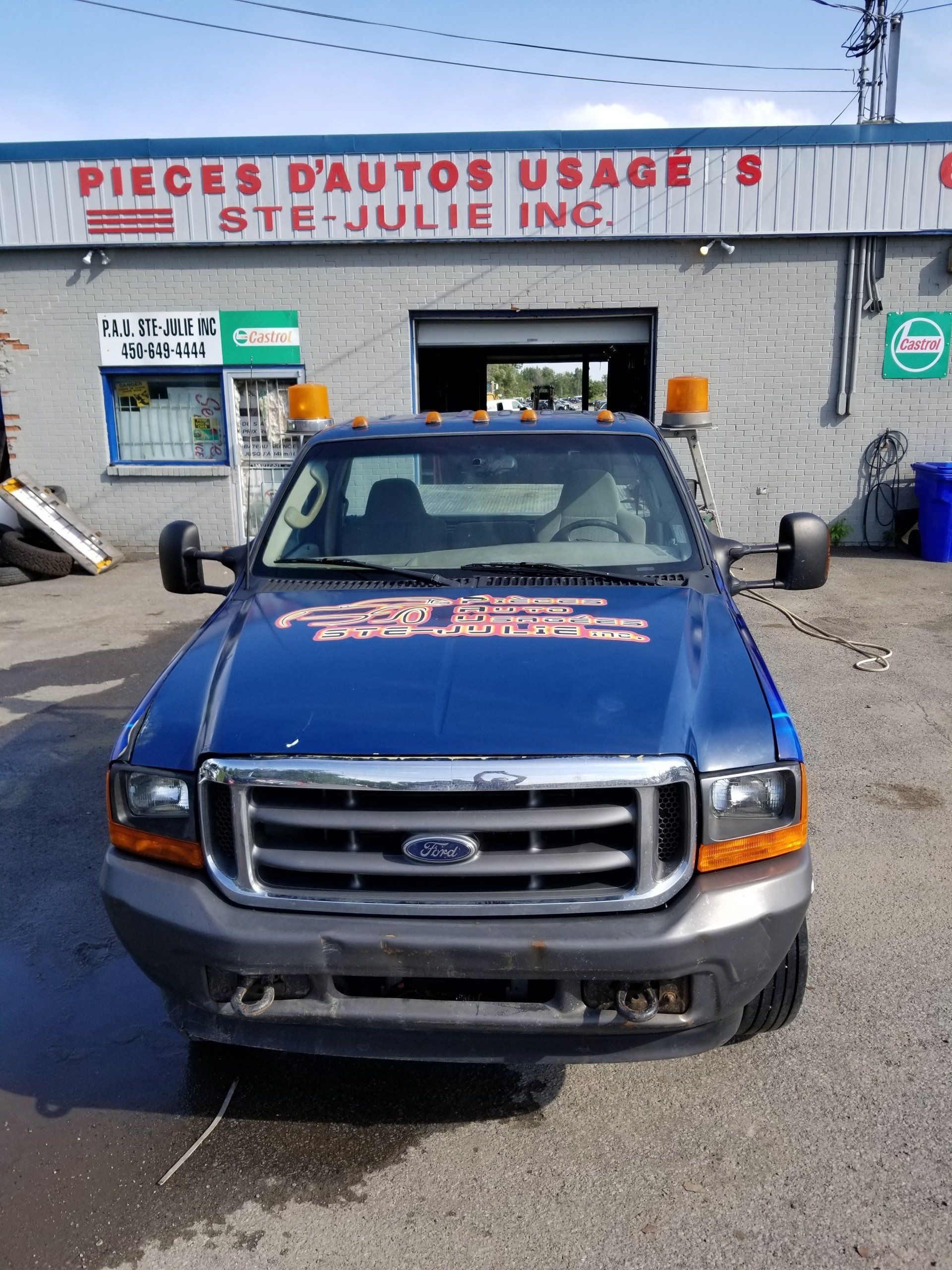 Un camion Ford bleu est garé devant l usage de Pieces d Autos