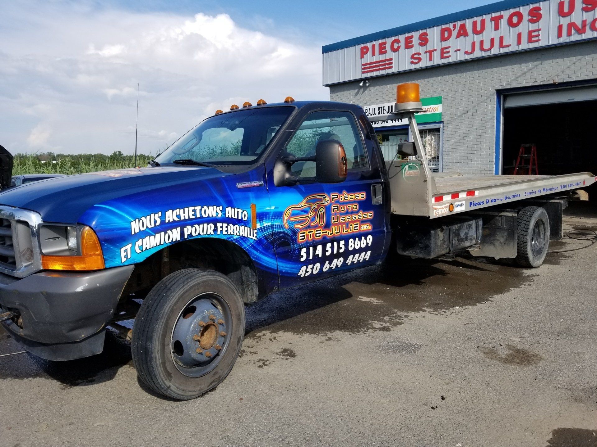 Une dépanneuse bleue est garée devant un bâtiment qui dit pièces d autos