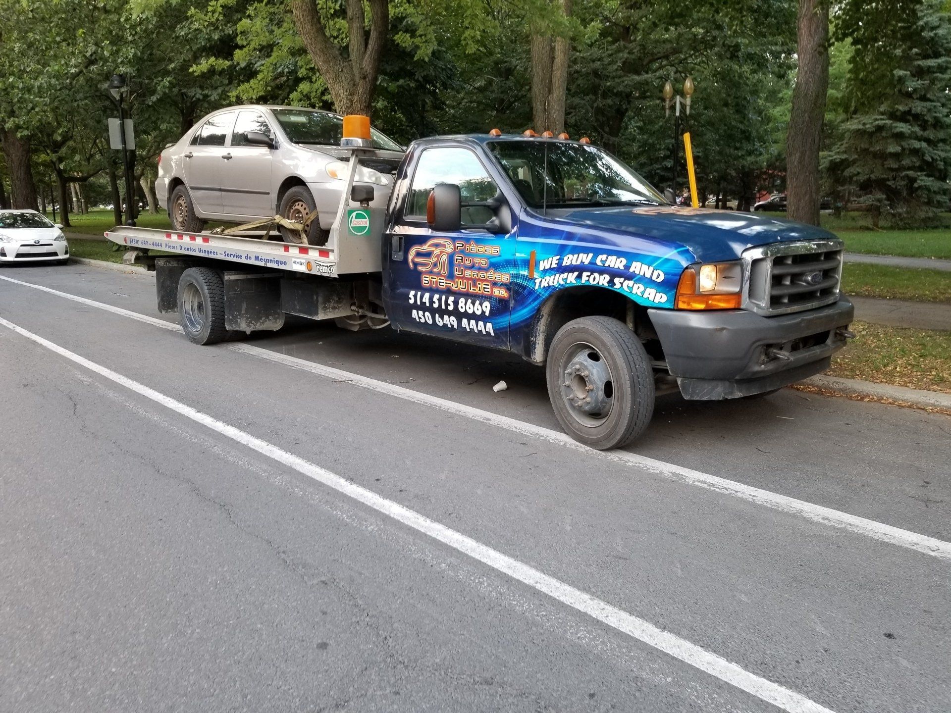 Une dépanneuse avec une voiture à l arrière est garée sur le bord de la route.