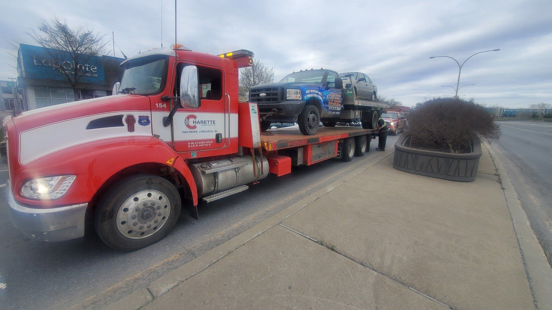 Une dépanneuse rouge remorque un camion bleu dans une rue.