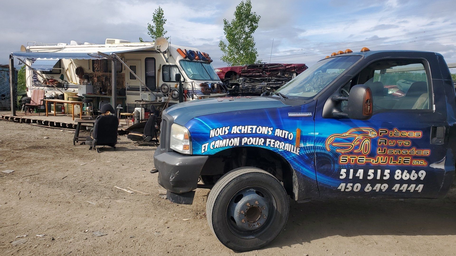 Un camion bleu est garé dans un terrain sale à côté d’un camping-car.