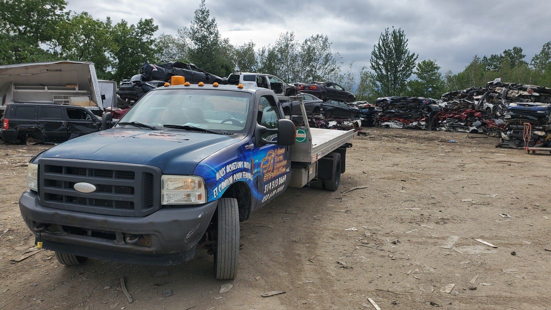 Une dépanneuse bleue est garée dans un tas de ferraille.