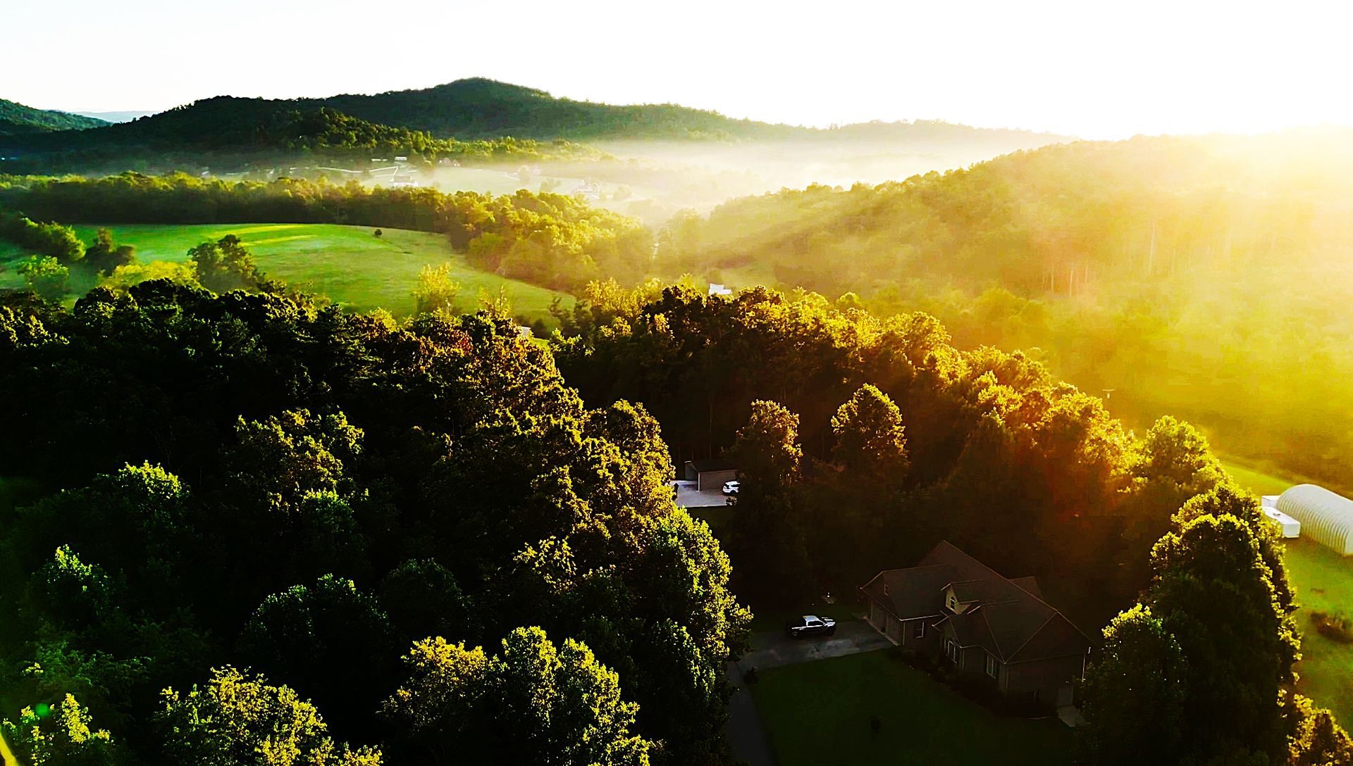 Golden sunrise over forested hills and a house.