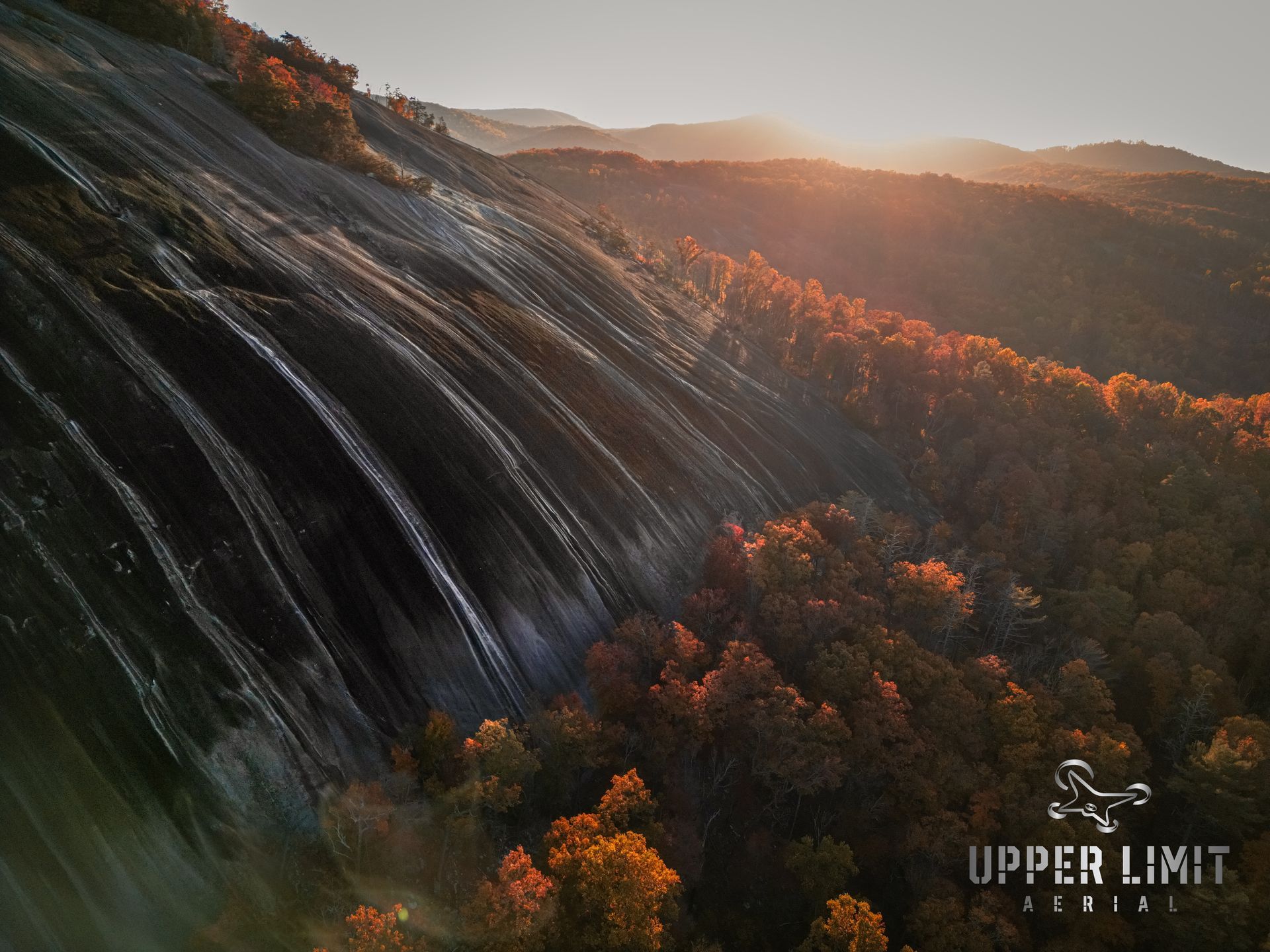 Sunset over a rocky mountain face with autumn foliage.