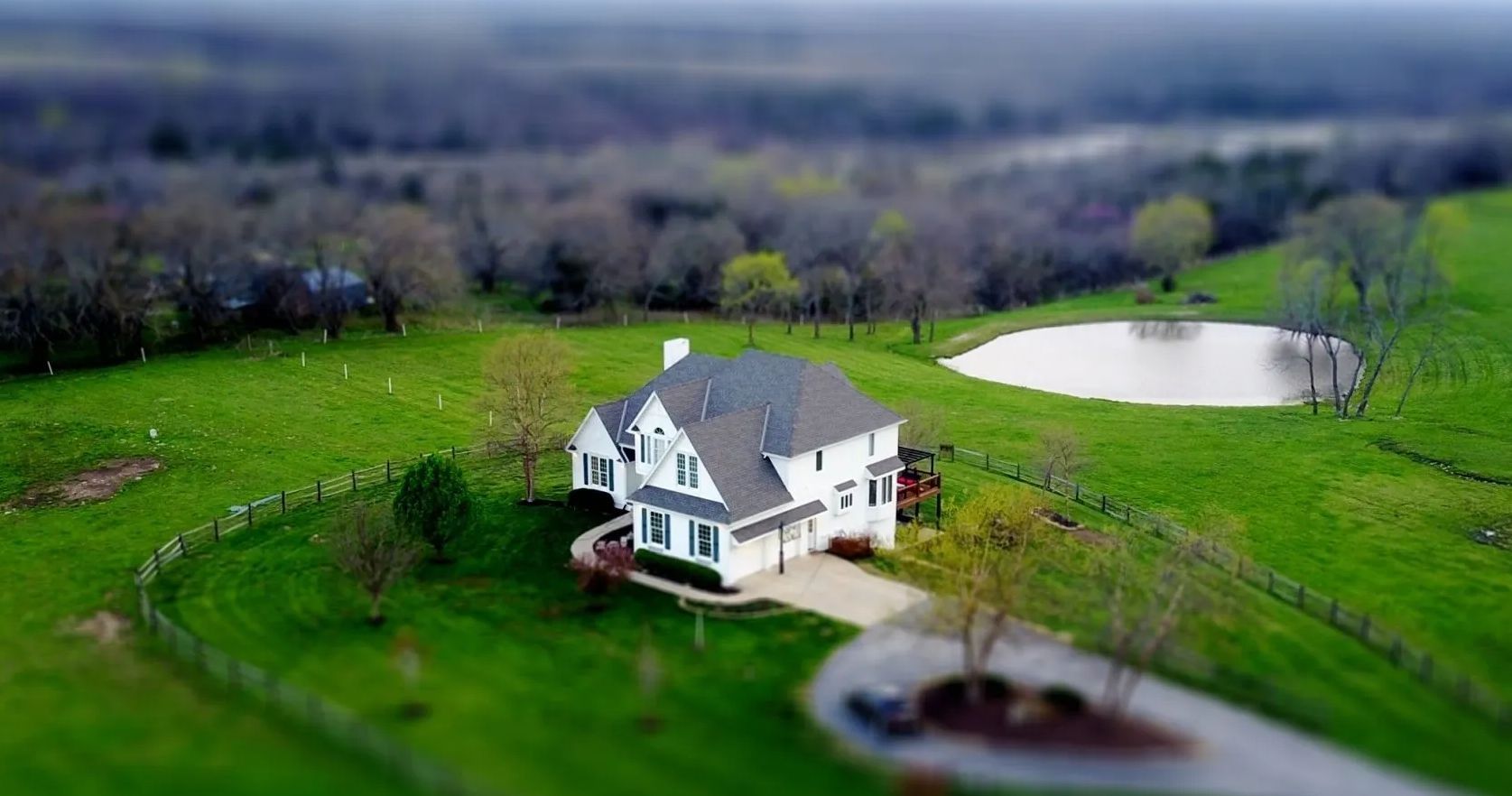 White house on a green hill with a pond and trees in the background, under an overcast sky.